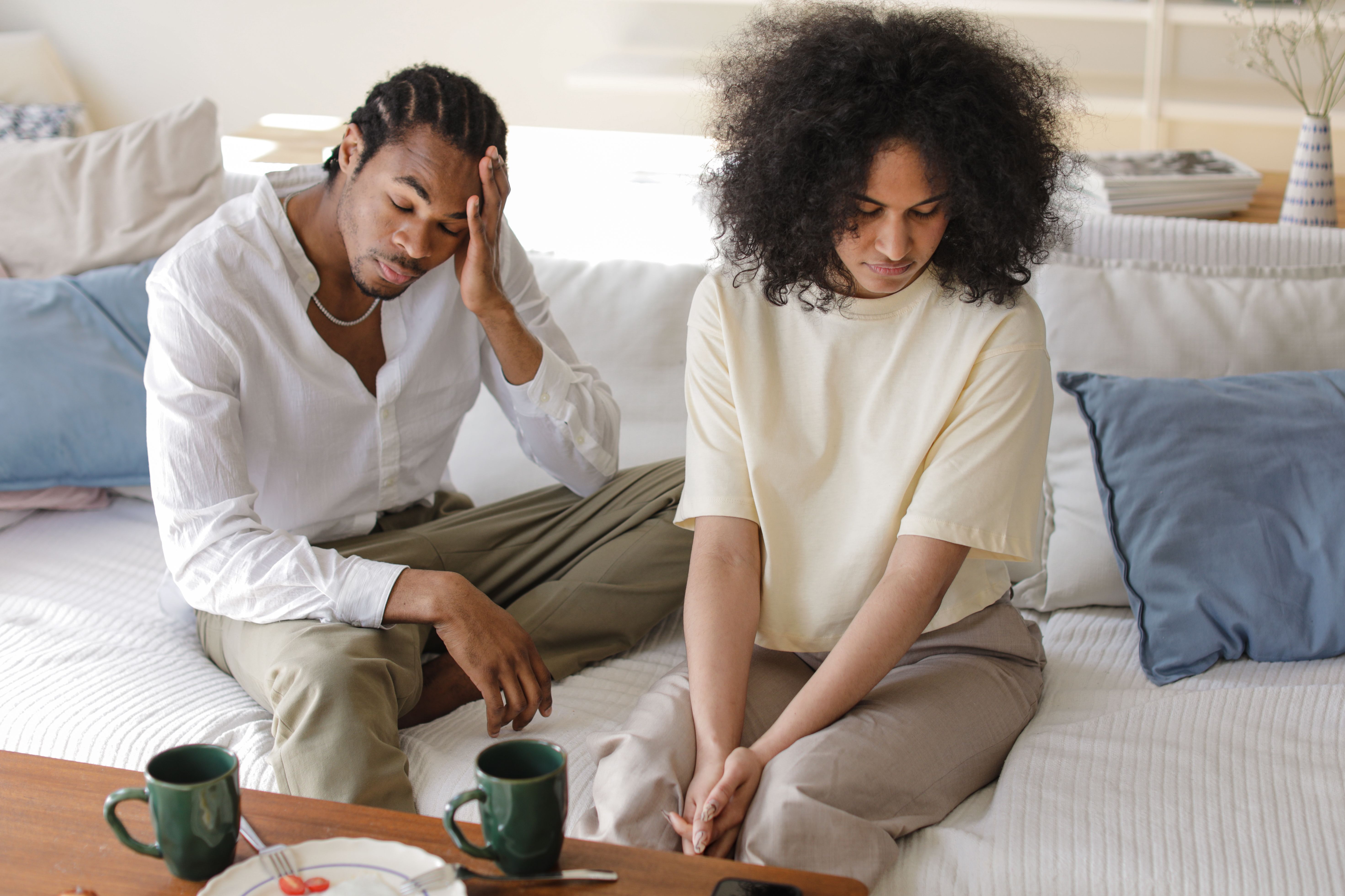 A contemplative black couple sitting on a sofa indoors in a modern setting, reflecting emotions.
